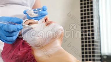 美容师将白色<strong>抗衰</strong>老面膜敷在脸上。 美的概念。 三十多岁的年轻女子在水疗中心